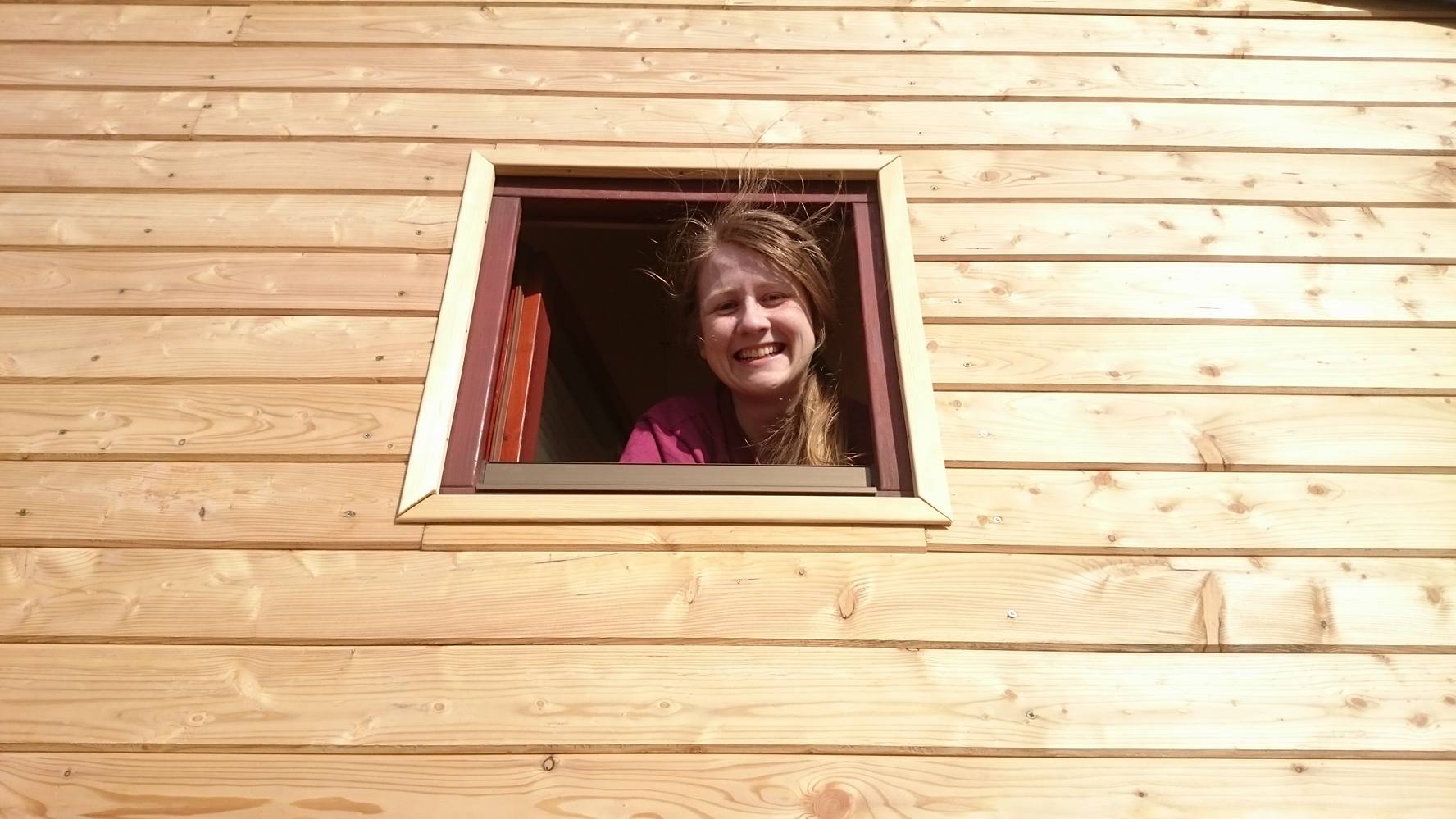 dievča pozrajúce sa von z maličkého okna v drevenej fasáde